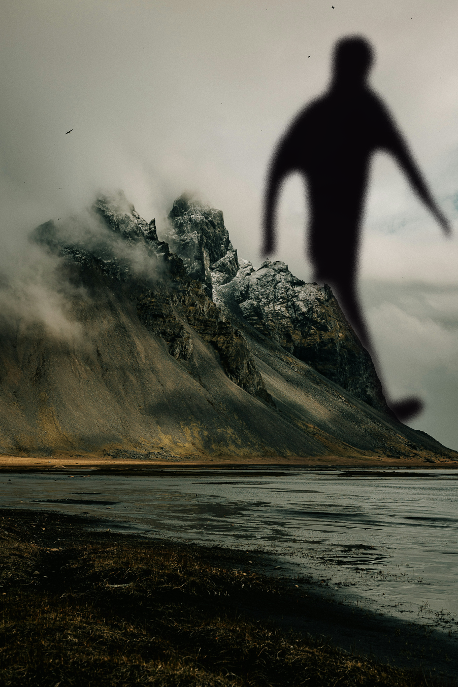 A mountain by the sea, behind which walks a distorted image of a humanoid figure.